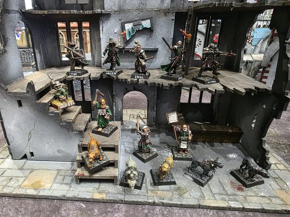 A painted Witch Hunter warband posed in a ruined Mordheim building: five witch hunters on the upper floor, a halfling on the stairs, three flagellants and five warhounds on the street